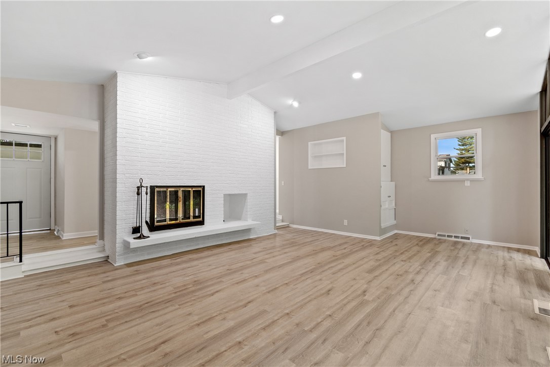 203 Pontius Road Mogadore, OH 44260 - Photo 19 of 26 Unfurnished living room featuring a fireplace, light hardwood flooring, and lofted ceiling with beams