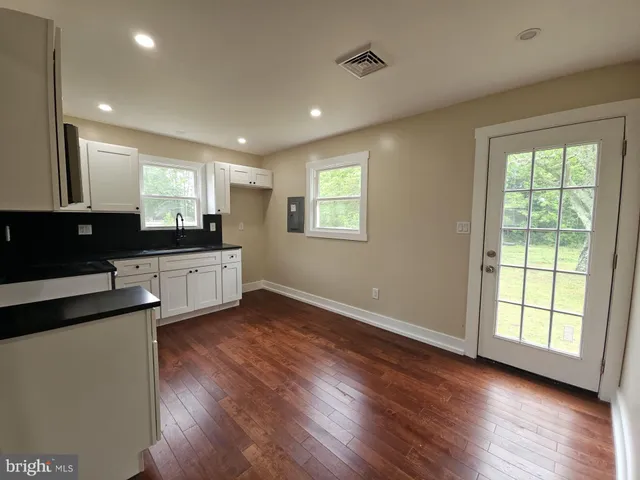 a large kitchen with stainless steel appliances granite countertop a stove a sink a refrigerator and white cabinets with wooden floor