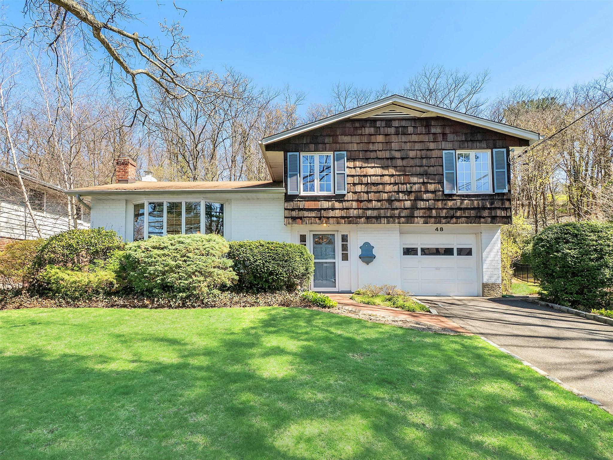 Split level home with a chimney, driveway, a front lawn, brick siding, and a garage
