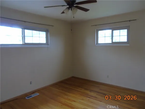an empty room with wooden floor fan and windows