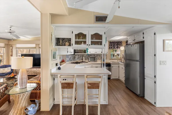 a kitchen with stainless steel appliances kitchen island granite countertop a refrigerator a stove a sink and white cabinets with wooden floor