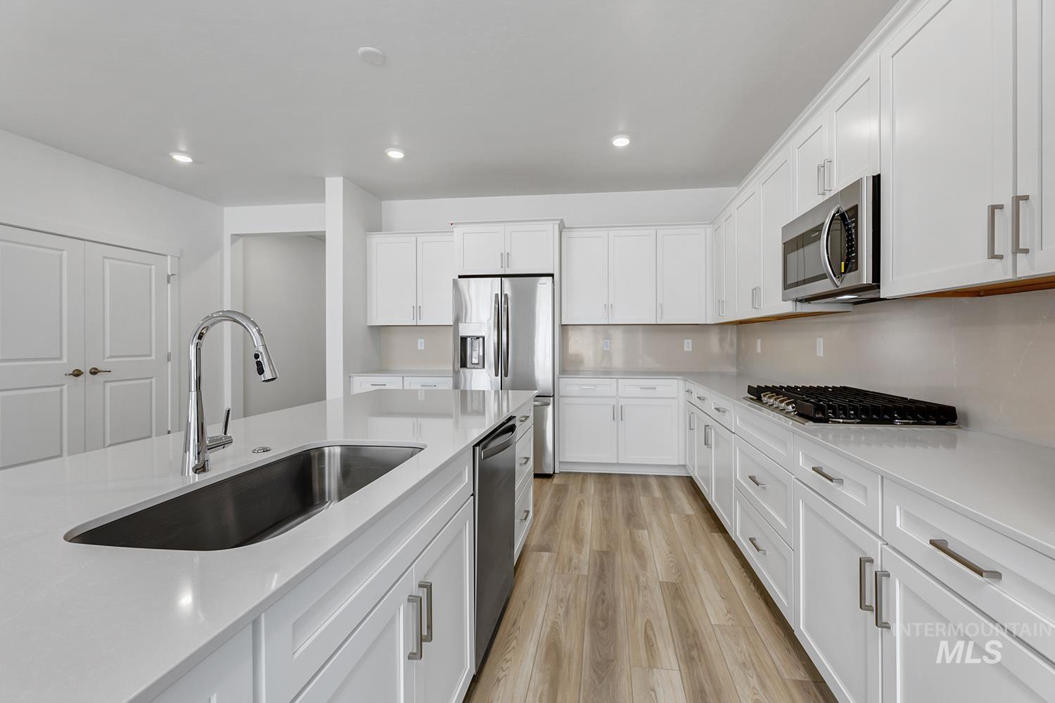 4548 West Wapoot Street Meridian, ID 83646 - Photo 10 of 17 Bright kitchen featuring an island with an undermount sink, white cabinetry with silver hardware, stainless steel appliances, wood-finish flooring, and recessed lighting