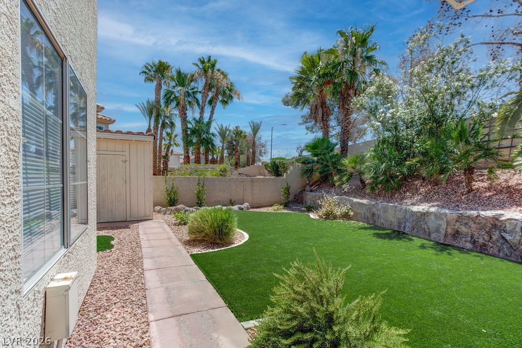 1 Rising Sun Court Henderson, NV 89074 - Photo 35 of 47 Green landscaping and palm trees create a peaceful desert oasis with a secluded shed.