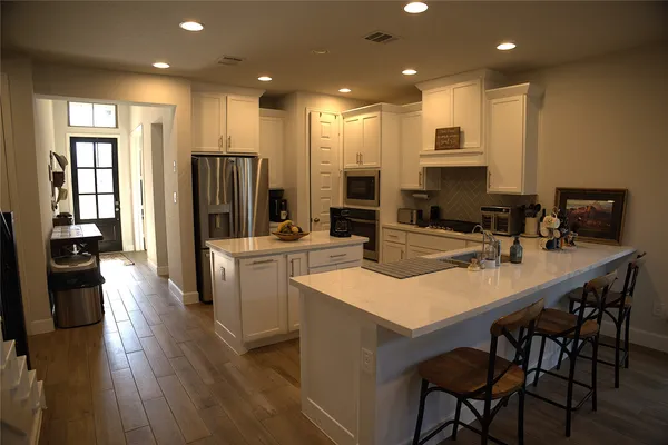 a kitchen with stainless steel appliances kitchen island granite countertop a refrigerator a stove a sink a dining table and chairs with wooden floor