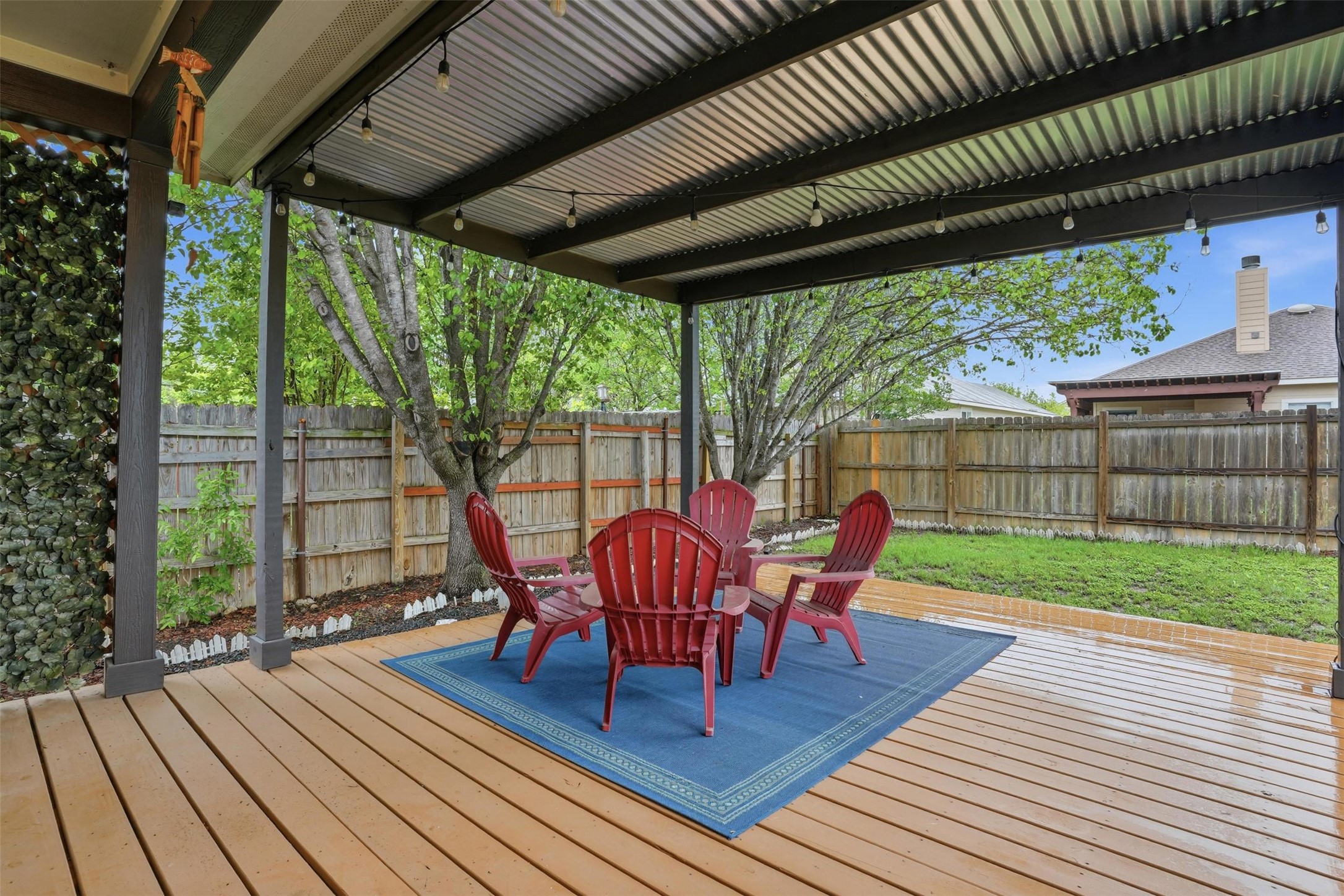 11606 Murchison Street Manor, TX 78653 - Photo 27 of 35 The property features a spacious outdoor deck with a corrugated metal patio cover, providing shade and strung lighting