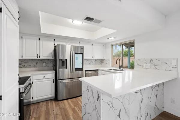 a kitchen with stainless steel appliances granite countertop a refrigerator a sink dishwasher a stove and white countertops with wooden floor