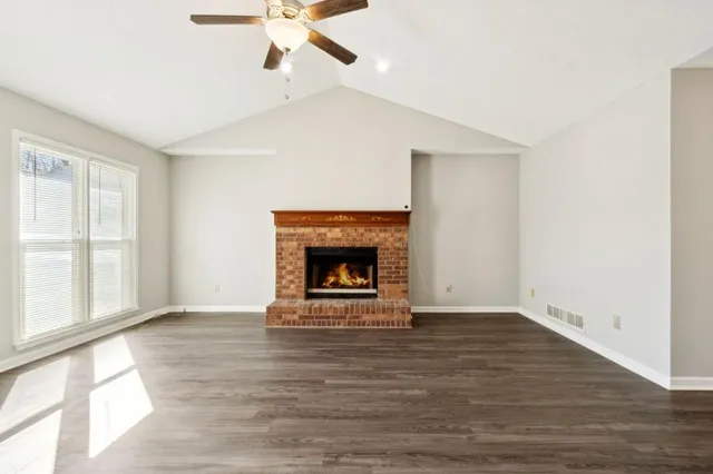 a view of an empty room with wooden floor fireplace and a window