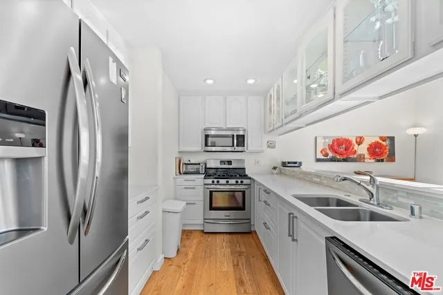 a kitchen with stainless steel appliances a refrigerator a sink a stove and white cabinets