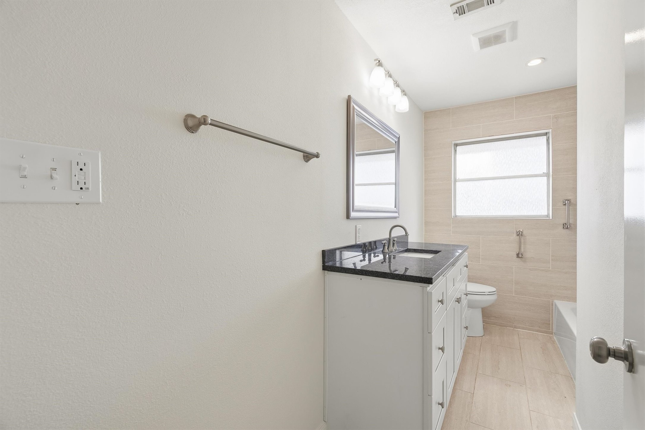 3331 Arbor Street Houston, TX 77004 - Photo 19 of 30 The updated guest bathroom features a modern design with a sleek black countertop, white vanity, and a large mirror. It has a tiled shower-tub combo and a window for natural light. Neutral tones create a clean and bright atmosphere.