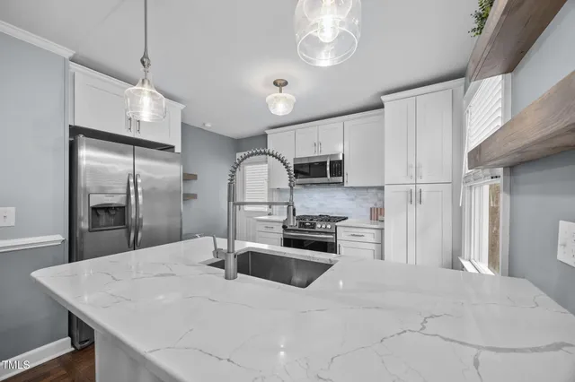 a kitchen with stainless steel appliances a sink a stove a refrigerator cabinets and chairs