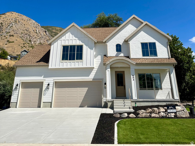 504 North 650 E Street Springville, UT 84663 - Photo 1 of 36 Contemporary residence featuring a clean white exterior with a combination of board and batten and brick finishes, a three-car garage, a concrete driveway, a manicured lawn, and a stone retaining wall