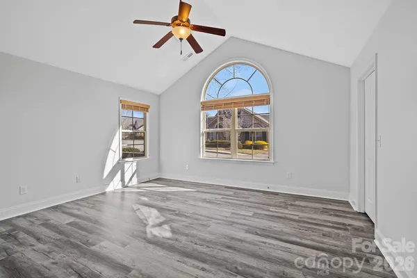 an empty room with wooden floor fan and windows