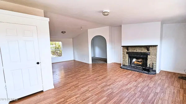 a view of an empty room with wooden floor fireplace and a window
