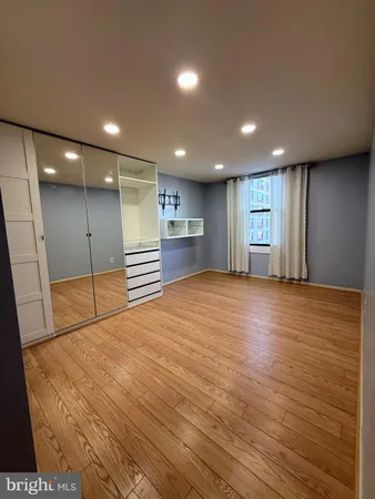 a view of an empty room with wooden floor and a kitchen