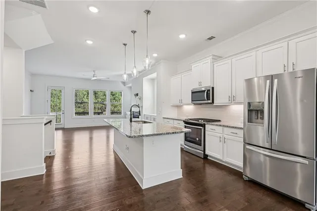 a kitchen with stainless steel appliances granite countertop a refrigerator a stove a sink cabinets and a wooden floor