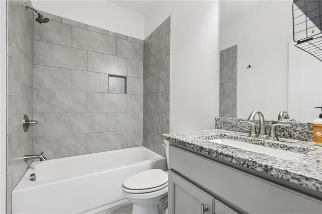 a bathroom with a granite countertop bathtub shower sink vanity mirror and toilet