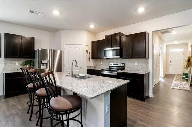 a kitchen with stainless steel appliances granite countertop a stove a refrigerator a sink a dining table and chairs