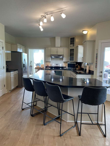 7030 West 2100 North Mendon, UT 84325 - Photo 25 of 67 Kitchen featuring a large island with dark countertop, light wood-finish flooring, white cabinetry, stainless steel appliances, and track lighting