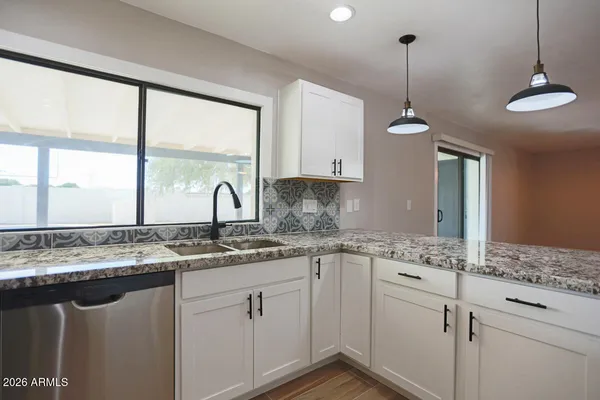 a kitchen with stainless steel appliances granite countertop a sink a window and white cabinets