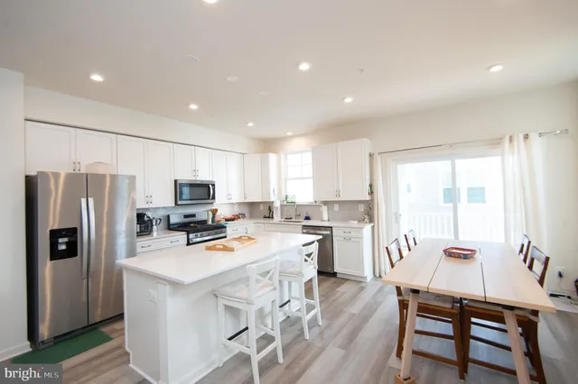 a kitchen with stainless steel appliances a refrigerator a stove a sink dishwasher a dining table and chairs with wooden floor