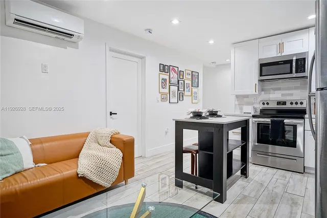 a living room with stainless steel appliances furniture a flat screen tv and kitchen view