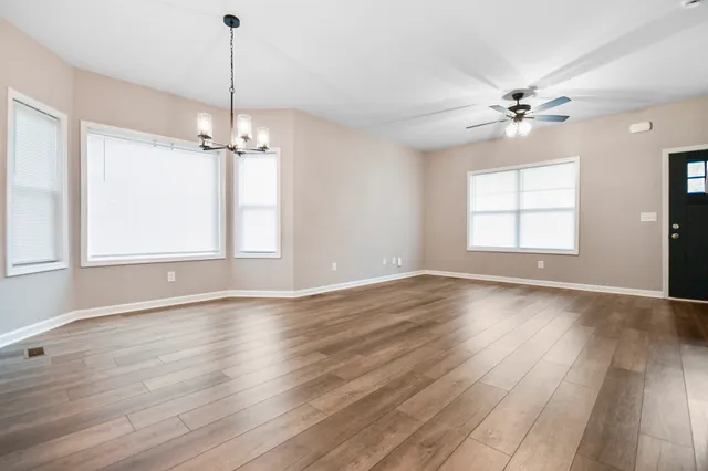 an empty room with wooden floor chandelier fan and windows