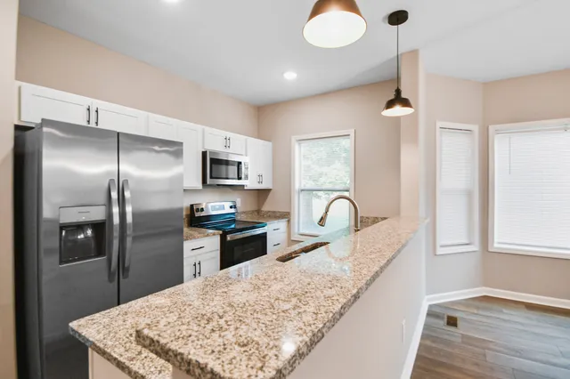 a kitchen with stainless steel appliances granite countertop a refrigerator a stove and a sink with wooden floor