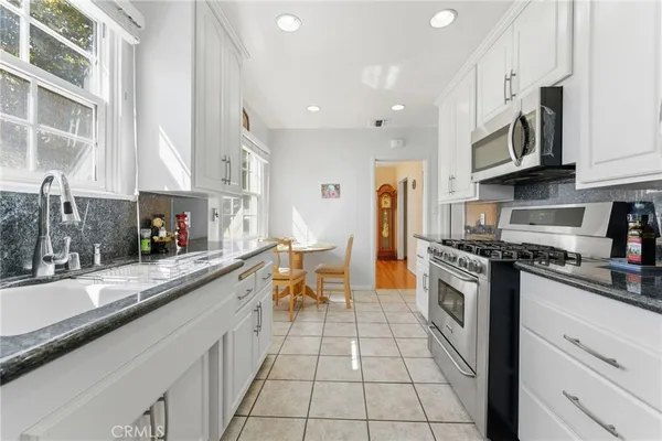 a large white kitchen with stainless steel appliances granite countertop a stove a sink a microwave and a refrigerator