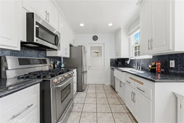 a kitchen with stainless steel appliances granite countertop a stove top oven a sink dishwasher and a refrigerator with wooden cabinets