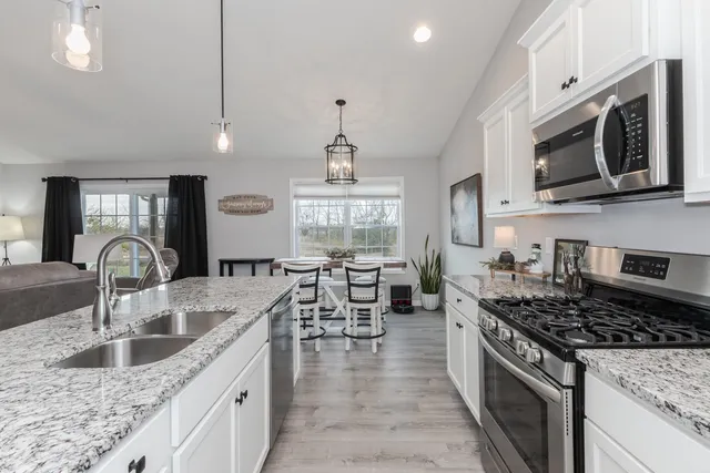 a kitchen with stainless steel appliances granite countertop a sink dishwasher stove and oven with white cabinets