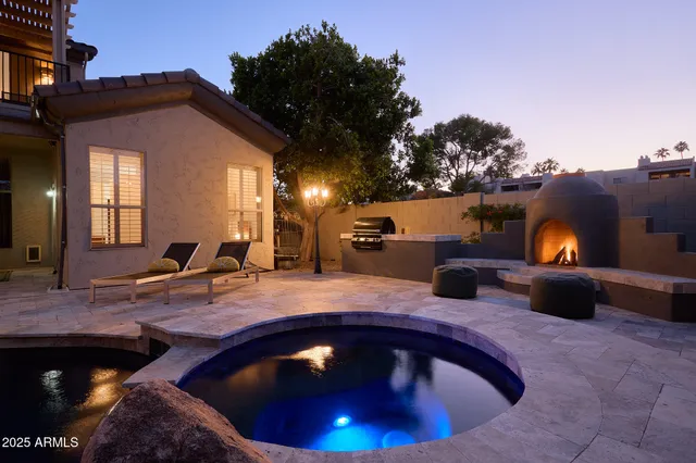 a view of a backyard with couches table and chairs under an umbrella with a fire pit