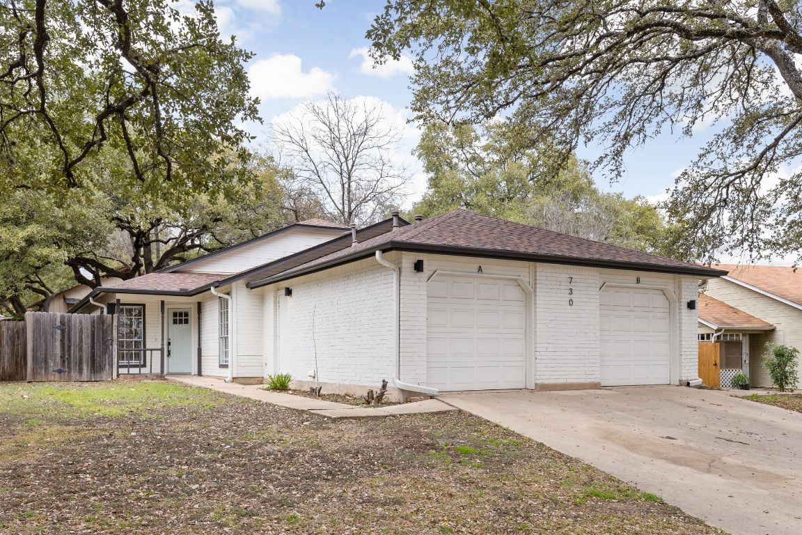 View of front facade featuring driveway, brick siding, an attached garage, and fence
