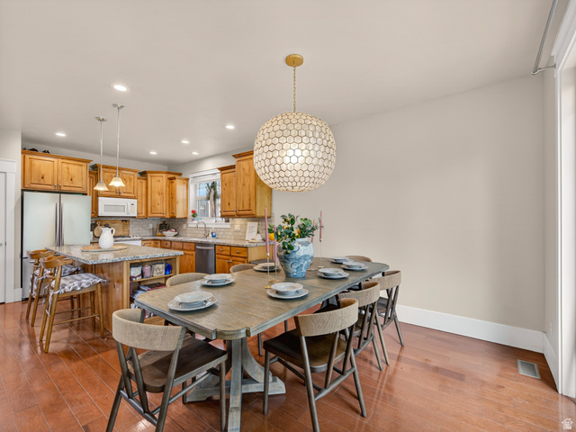 557 Craftsman Way Midway, UT 84049 - Photo 14 of 59 Open-concept dining area featuring wood-finish flooring, a contemporary spherical chandelier, and a kitchen with wood cabinetry, a center island with bar seating, and a granite countertop
