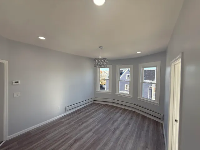 a view of an empty room with wooden floor and window