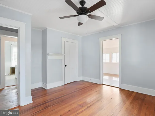 a view of an empty room with wooden floor and a ceiling fan