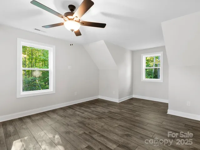 an empty room with wooden floor fan and windows
