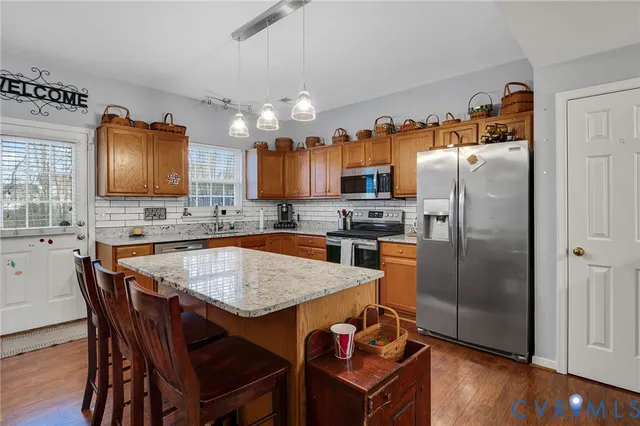 a kitchen with granite countertop a refrigerator a stove a sink dishwasher a dining table and chairs with wooden floor