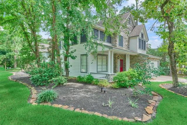 a view of a big yard in front of a brick house with plants and large trees