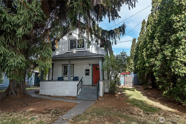 a view of a white house with a large tree and wooden fence