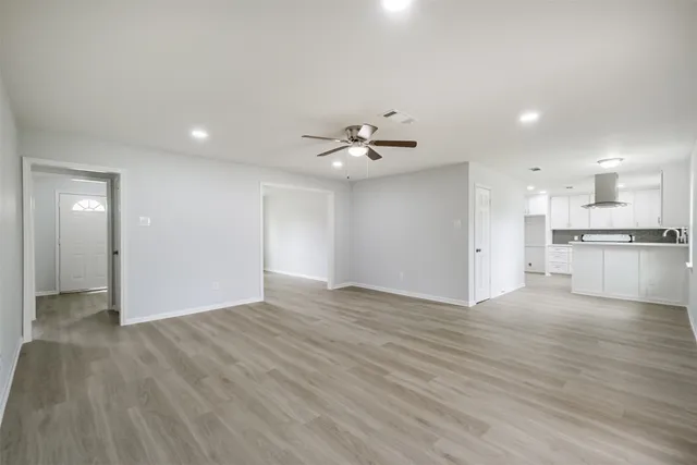 a view of an empty room and kitchen view with wooden floor