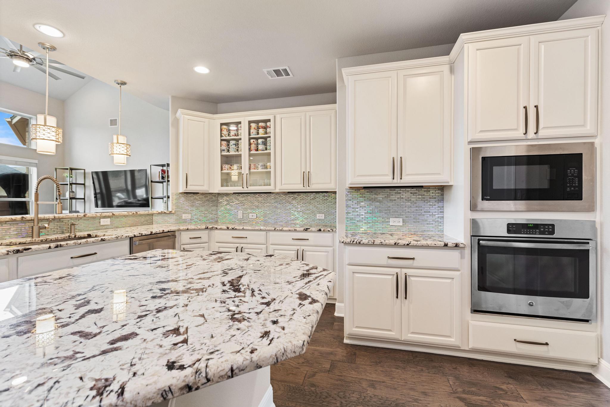 3028 Silvergrass Cove Leander, TX 78641 - Photo 13 of 38 Kitchen featuring decorative light fixtures, stainless steel appliances, decorative backsplash, light stone counters, and glass insert cabinets