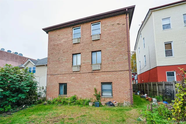 a view of a brick house with a yard plants and large tree