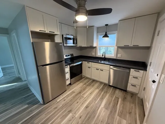 a kitchen with granite countertop a refrigerator a sink and white cabinets