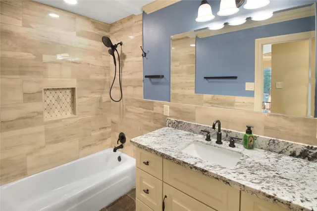 a bathroom with a granite countertop sink a mirror and a bathtub with shower