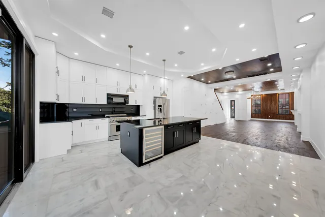 a kitchen with stainless steel appliances kitchen island granite countertop a stove a sink a refrigerator and white cabinets with wooden floor