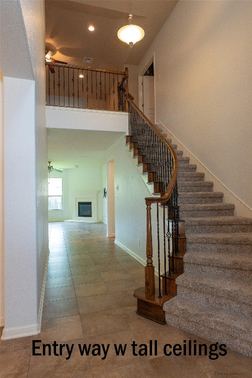 104 Palisades Cove Austin, TX 78732 - Photo 23 of 27 Stairs with a glass covered fireplace, a ceiling fan, and a high ceiling