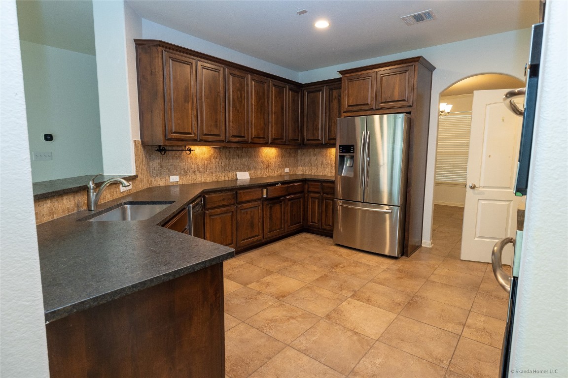 104 Palisades Cove Austin, TX 78732 - Photo 9 of 27 Kitchen with dark countertops, arched walkways, stainless steel appliances, tasteful backsplash, and dark brown cabinetry