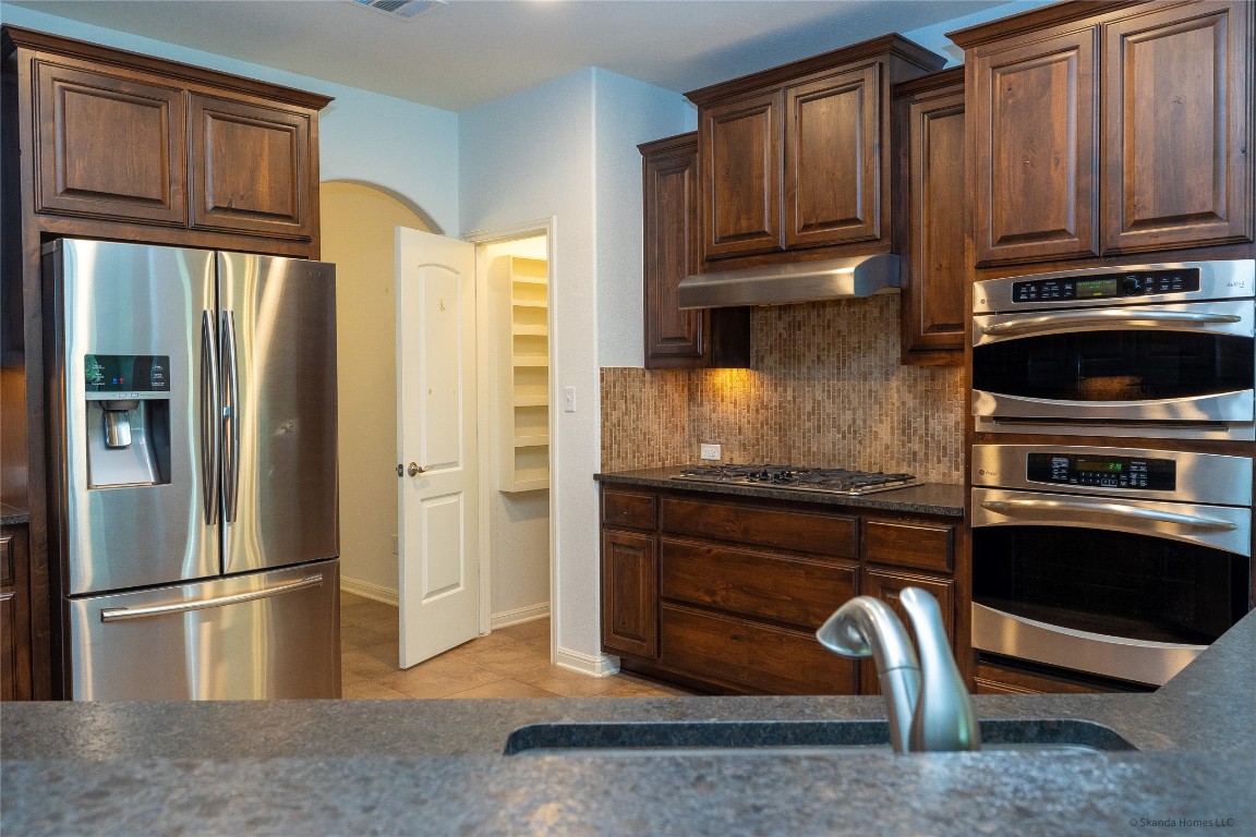 104 Palisades Cove Austin, TX 78732 - Photo 10 of 27 Kitchen with stainless steel appliances, decorative backsplash, light tile patterned floors, under cabinet range hood, and arched walkways