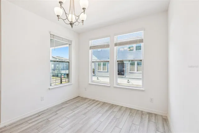 an empty room with wooden floor chandelier and windows