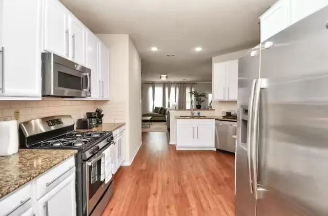 a kitchen with stainless steel appliances kitchen island granite countertop a stove a sink dishwasher and a refrigerator with wooden floor